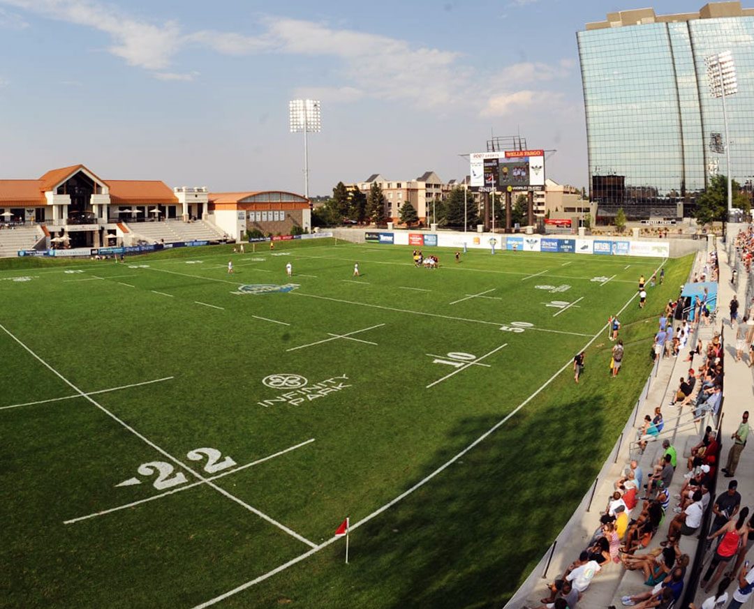 Wide view of Infinity Park rugby stadium in Denver with spectators in the stands and players on the field.